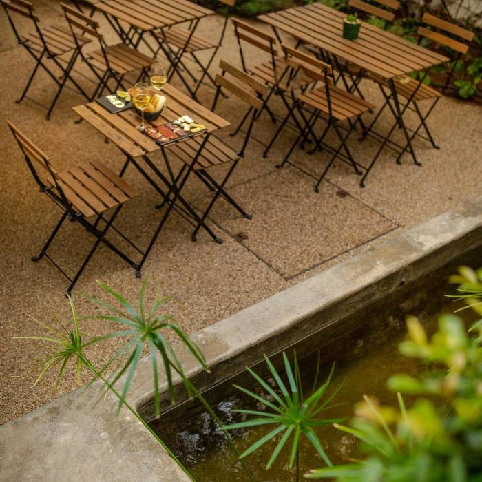 Mesa com bebidas em &aacute;rea externa, com cadeiras de ferro e plantas ao fundo.