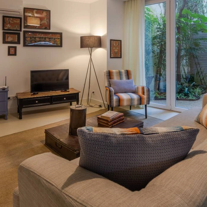 Sala de estar moderna com sof&aacute;, TV e luz natural pela janela.