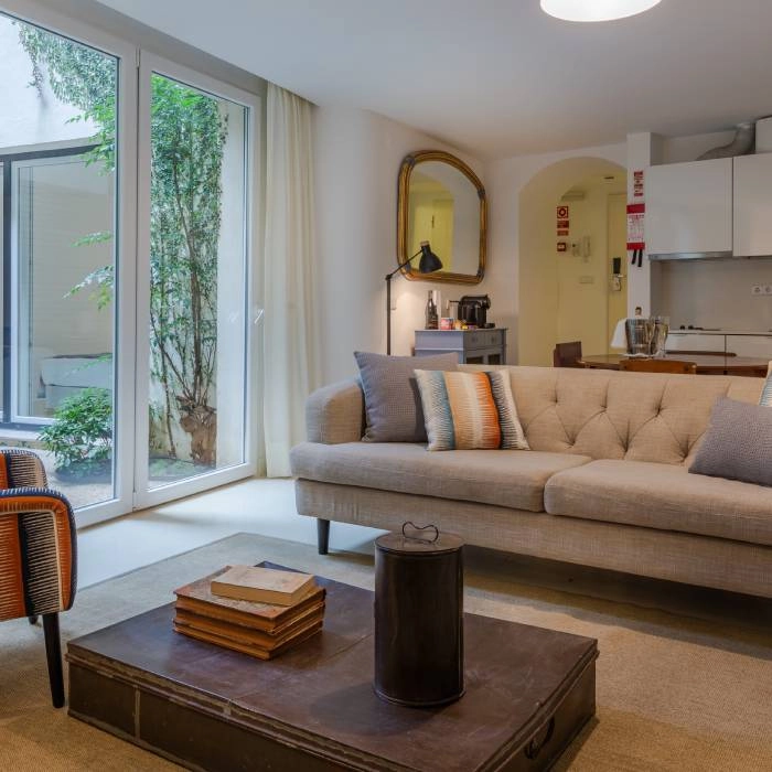 Sala de estar moderna com sof&aacute;, mesa e cozinha integrada, com luz natural.