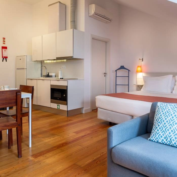 Est&uacute;dio moderno com sof&aacute; azul, cama e cozinha compacta com ar-condicionado