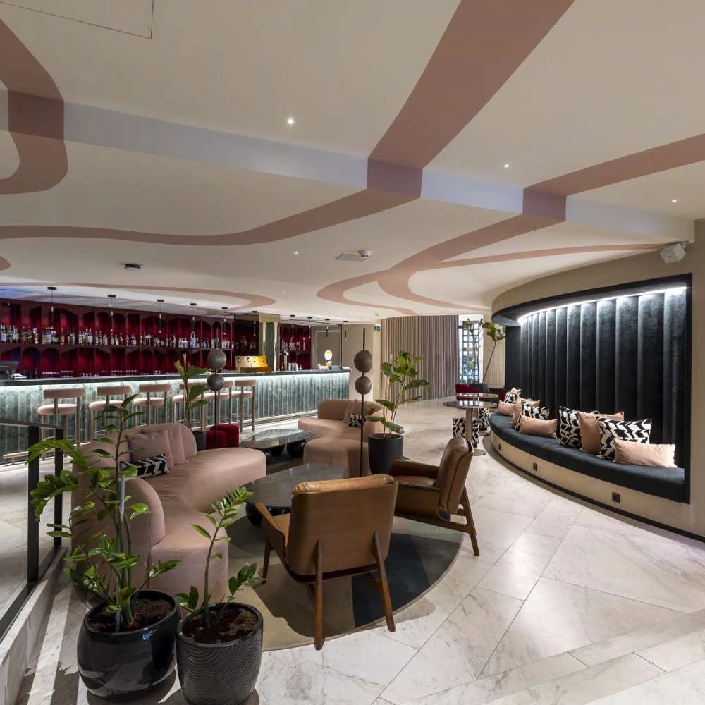 Modern lounge with bar, armchairs, and plants in an elegant environment.