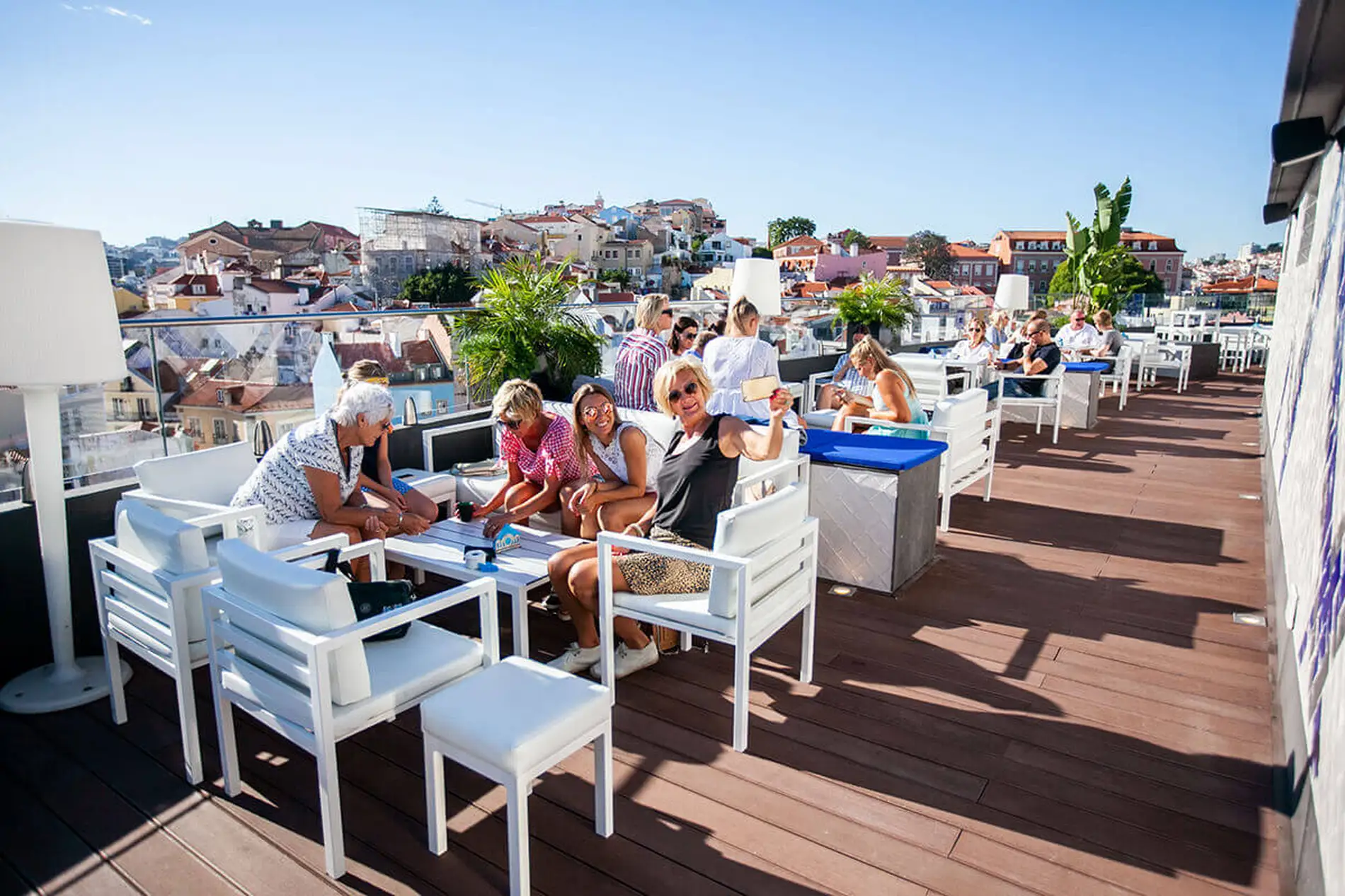 Grupo de personas relaj&aacute;ndose en una terraza con vistas a la ciudad bajo el sol