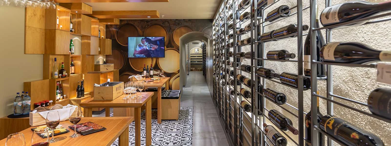 Adega climatizada com fileiras de vinhos, mesa de degusta&ccedil;&atilde;o e TV ao fundo