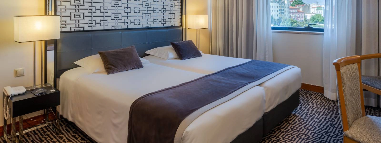 Quarto de hotel moderno com cama king, almofadas e cortinas claras