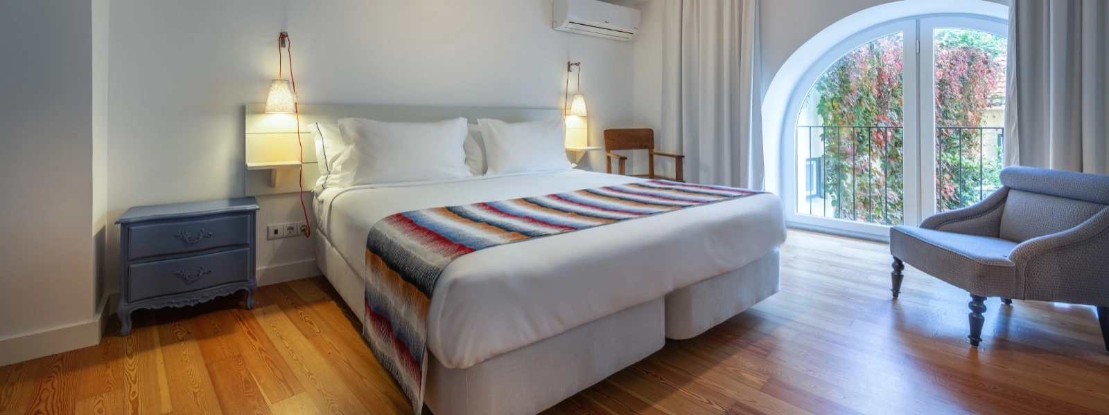 Quarto moderno com cama de casal, poltrona e janela em arco com luz natural