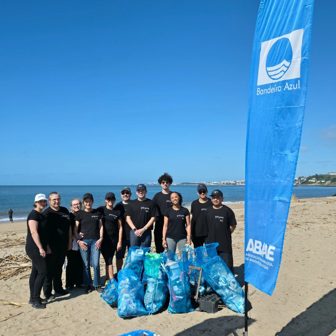 Team am Strand mit blauer Flagge und M&uuml;lls&auml;cken zum Recycling
