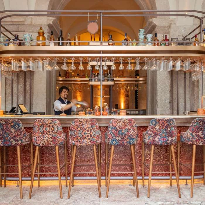 Barman serves cocktails in an elegant bar with colorful chairs and glasses.
