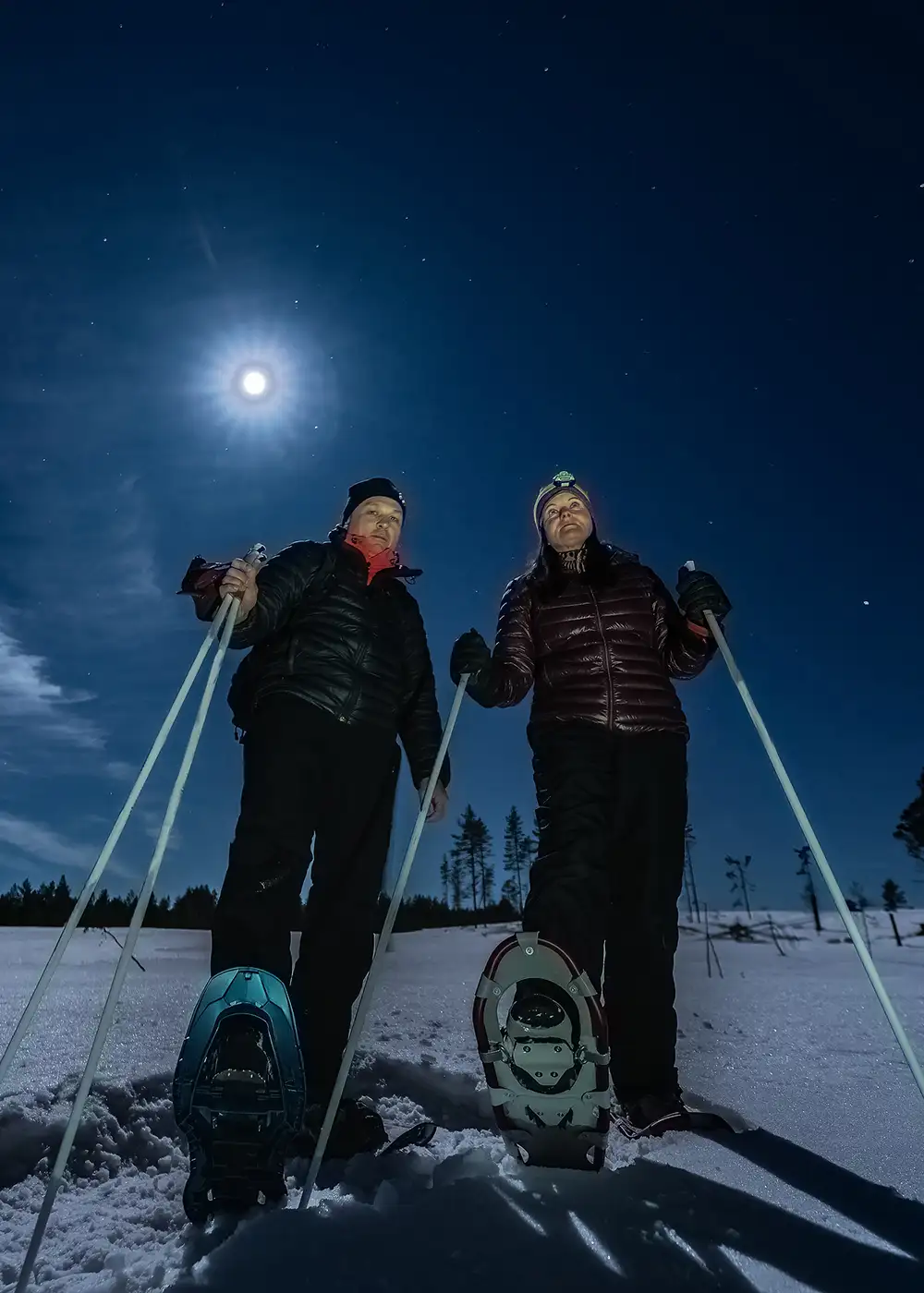 Dos esquiadores con esqu&iacute;s bajo luna brillante en la nieve nocturna