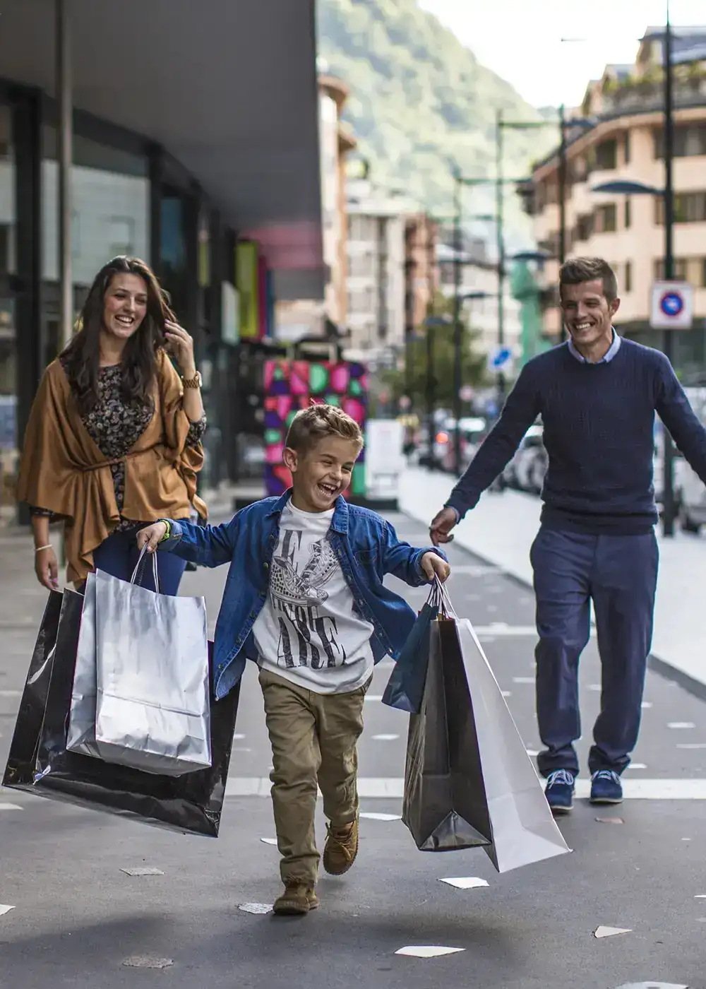Familia caminando por la calle con bolsas de compras, ni&ntilde;o feliz al frente