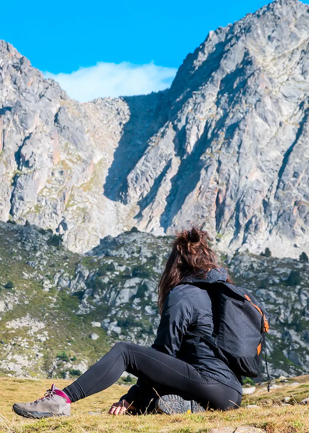 Persona sentada con mochila ante monta&ntilde;as rocosas y cielo azul