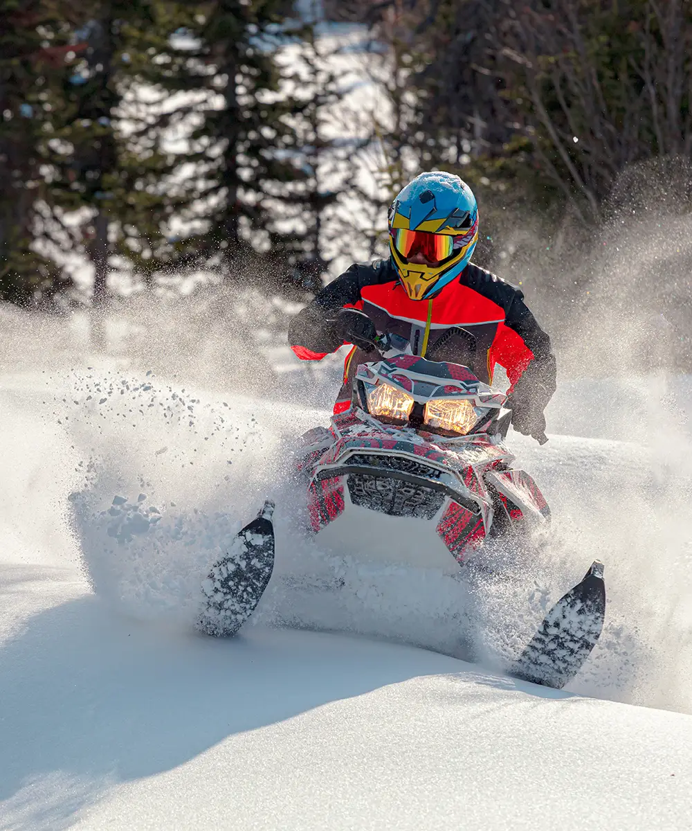 Motociclista con casco azul y rojo saltando en moto bajo nieve, con polvo.