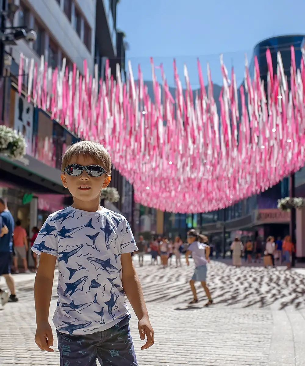 Ni&ntilde;o con gafas, camiseta con tiburones, en calle con banderines rosa