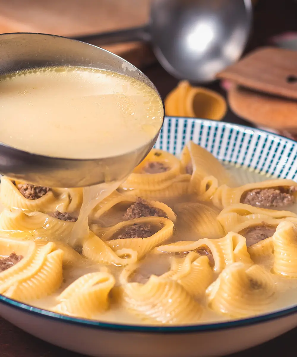 Pasta en plato hondo con salsa y trozos de carne, vertiendo de una sart&eacute;n