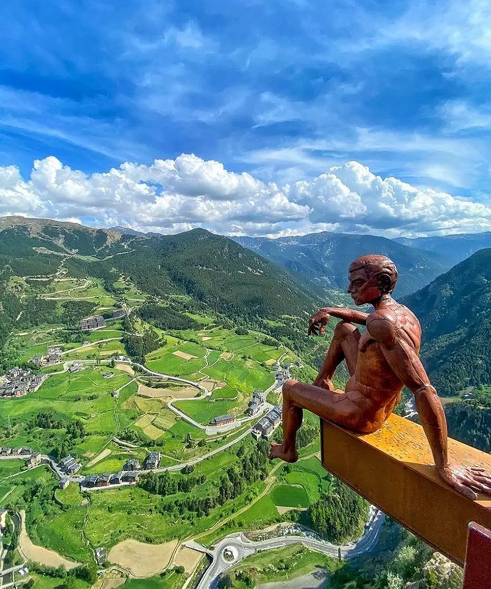 Escultura desnuda sobre mirador con valle verde y nubes en el cielo