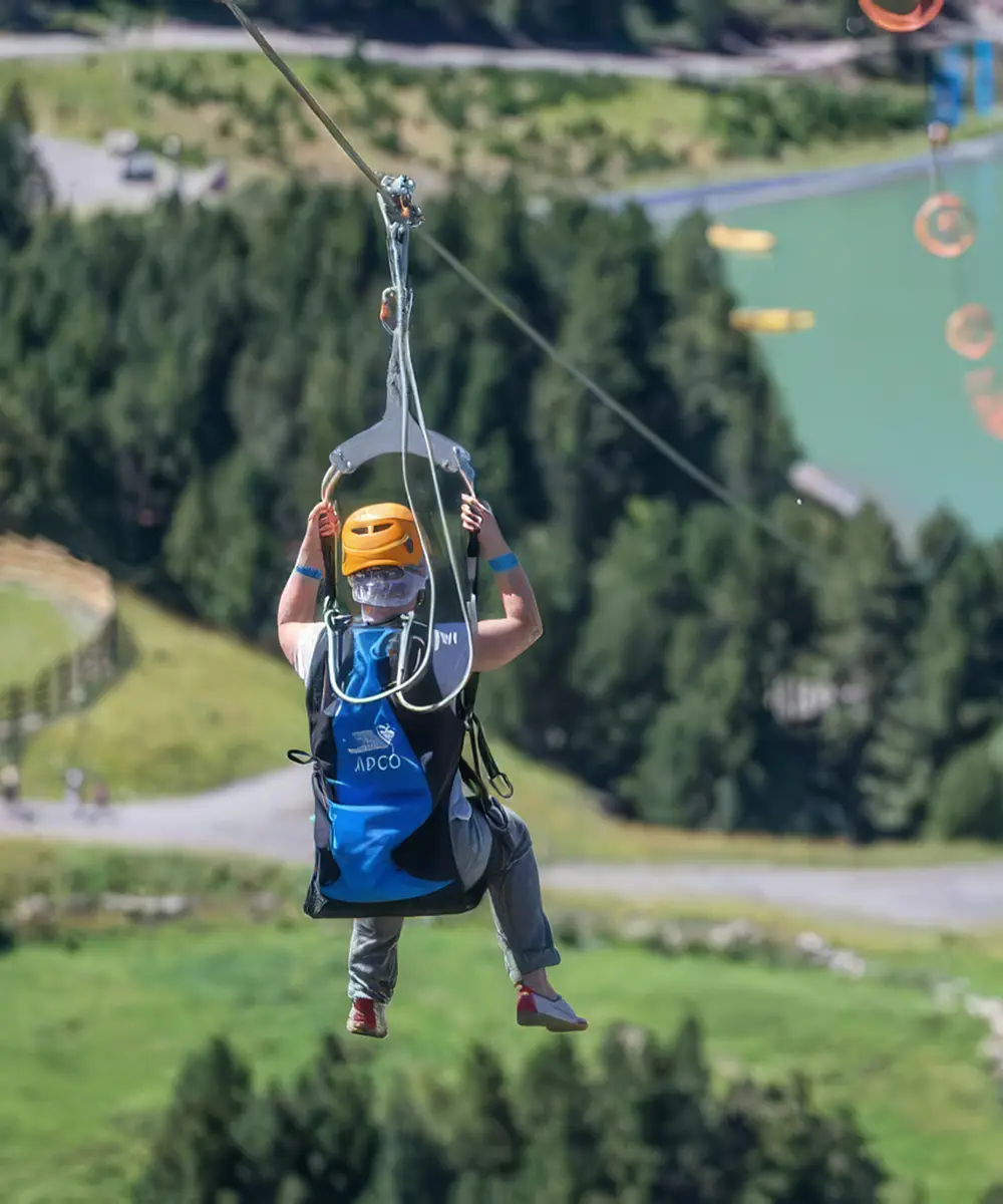 Persona volando con arn&eacute;s y cuerda sobre un valle, en parapente/tirolesa.