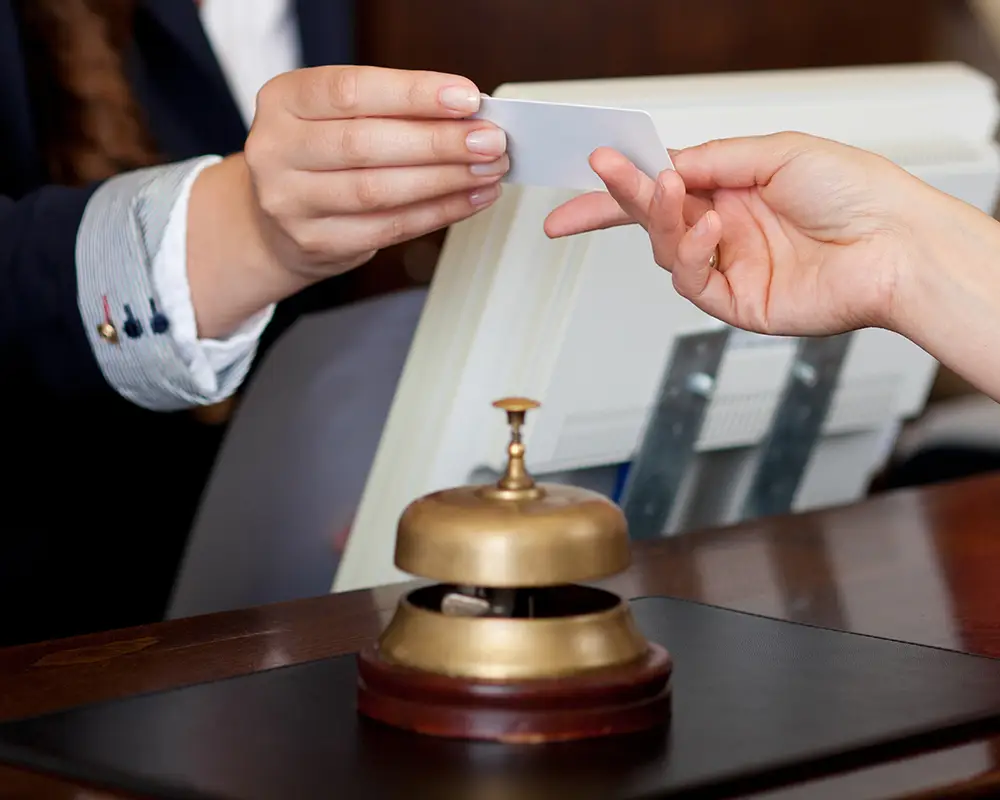 Dos manos entregando una tarjeta en un mostrador con un timbre de recepci&oacute;n