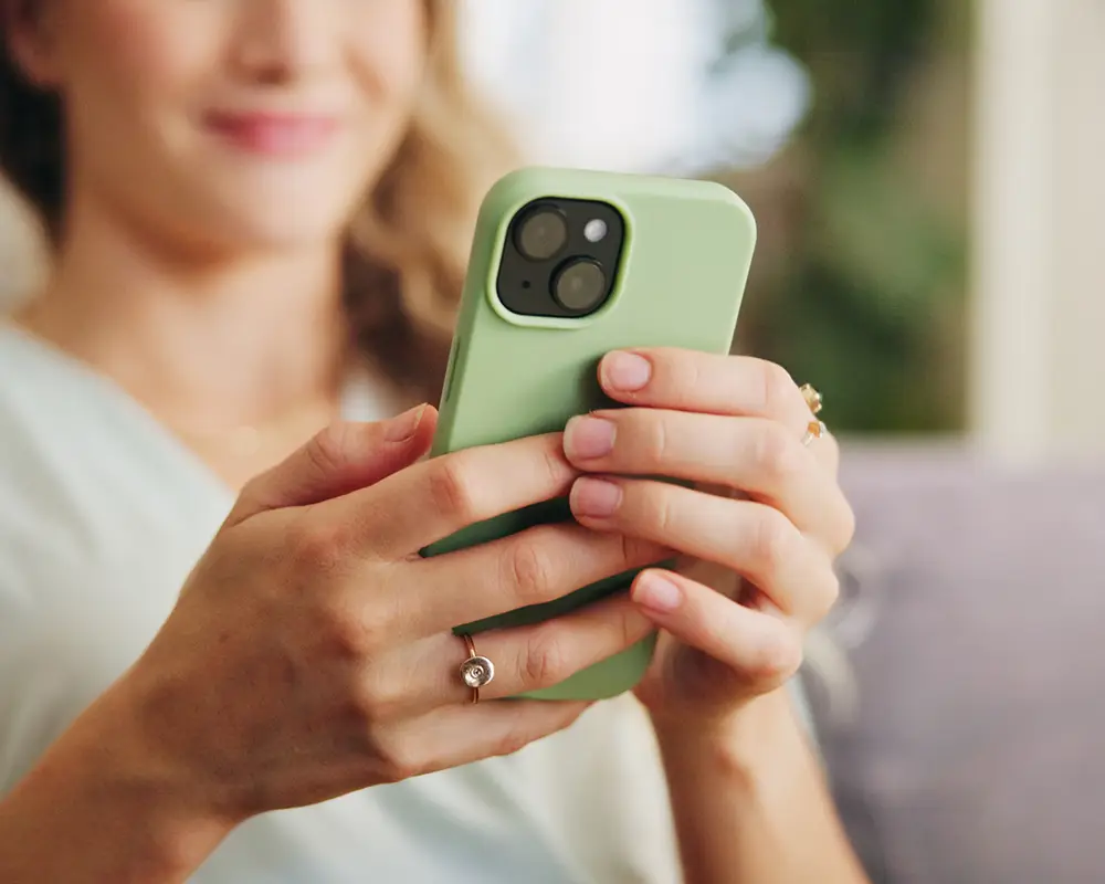 Persona sostiene un smartphone verde mientras otra mano lo toca, al aire libre.
