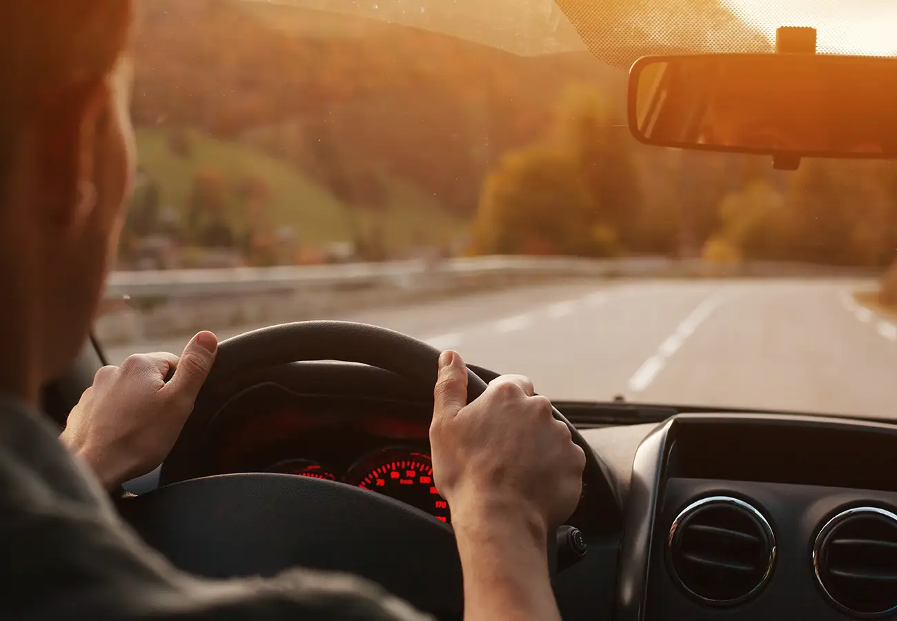 Conducci&oacute;n por carretera, manos al volante con el camino al frente.