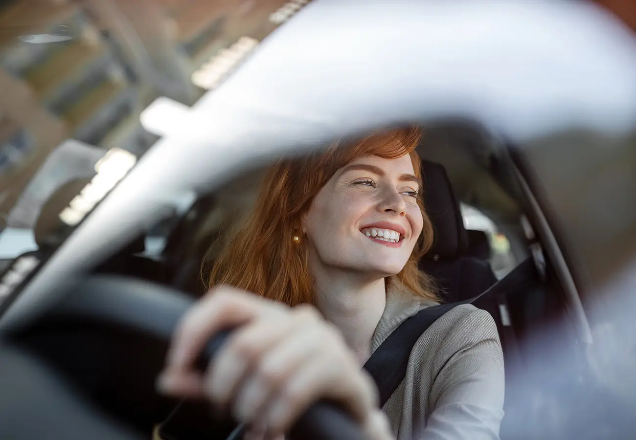 Mujer sonriente al volante de un coche, con el brazo extendido hacia adelante