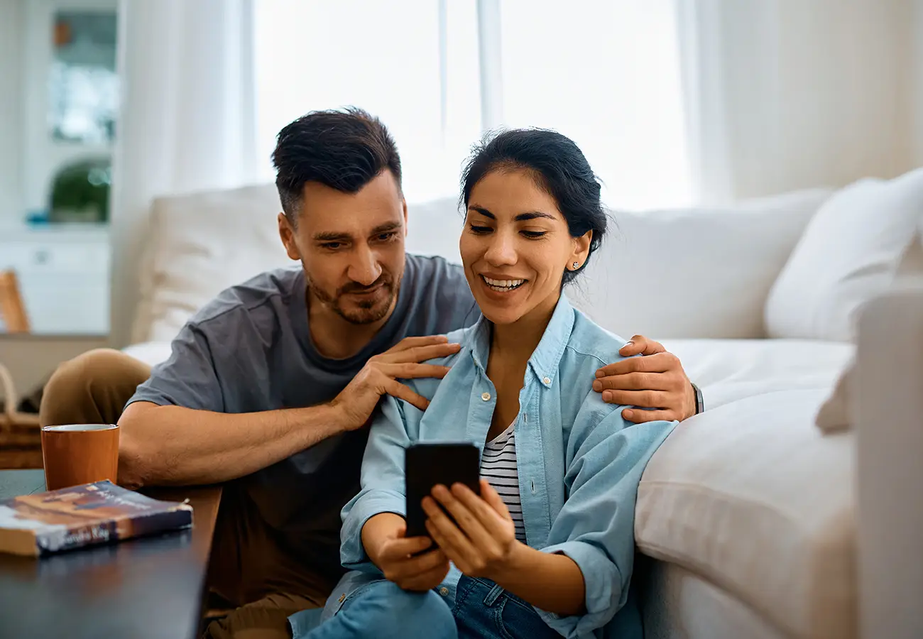 Pareja en el sof&aacute; riendo mientras mira un tel&eacute;fono juntos
