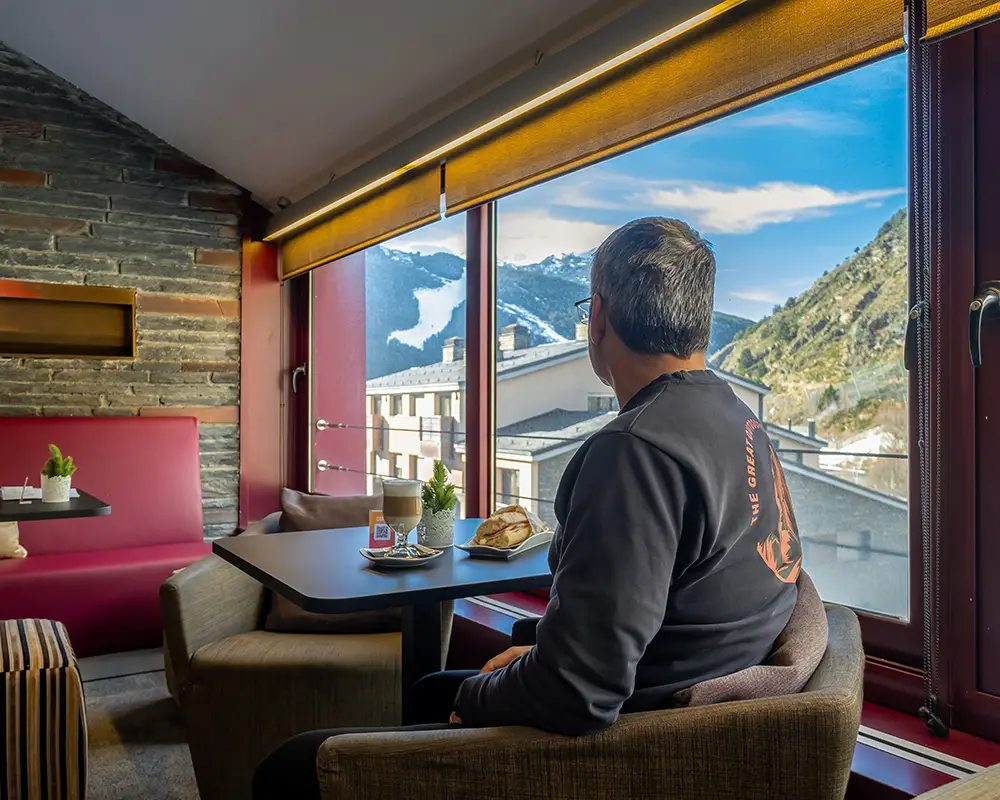 Hombre sentado junto a ventanal con monta&ntilde;as y mesa en un hotel