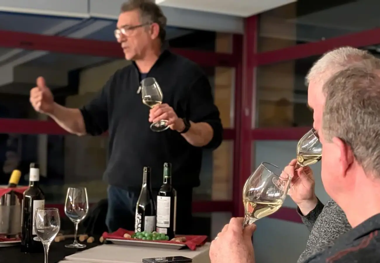 Cata de vino: hombre brinda con copa en una mesa con botellas y asistentes