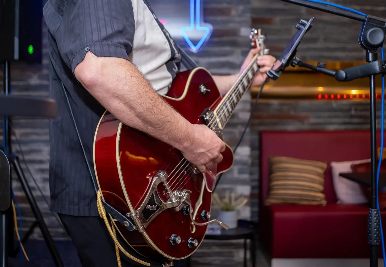 M&uacute;sico tocando guitarra roja en escenario con micr&oacute;fono y luces azules