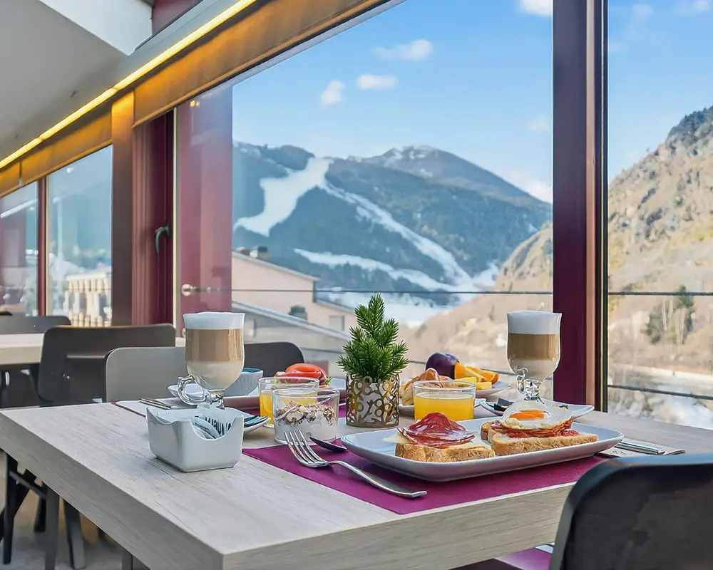 Mesa de desayuno con vino y vista a monta&ntilde;as nevadas desde un comedor moderno