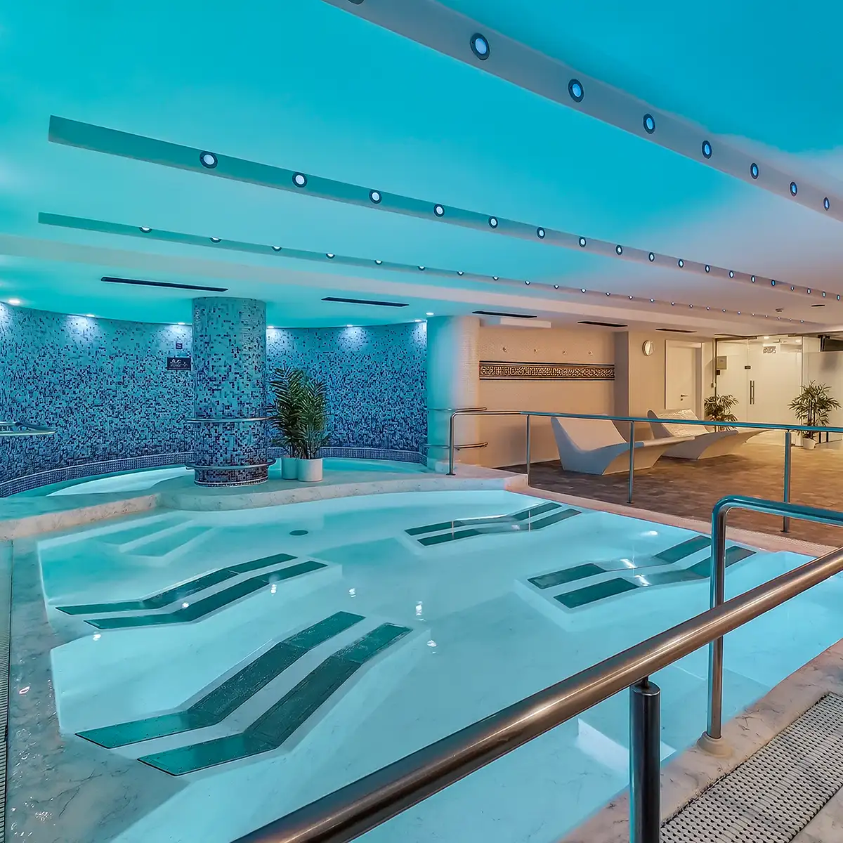 Piscina cubierta turquesa con paneles de mosaico y techo de cristal.