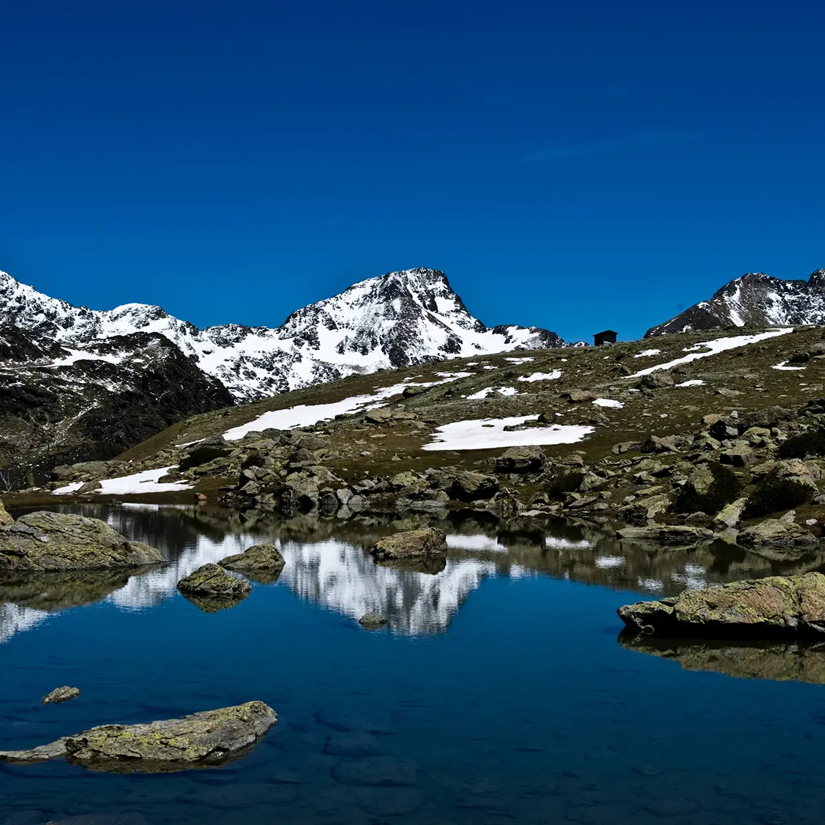 Monta&ntilde;as nevadas con lago tranquilo y cielo azul, en paisaje alpino