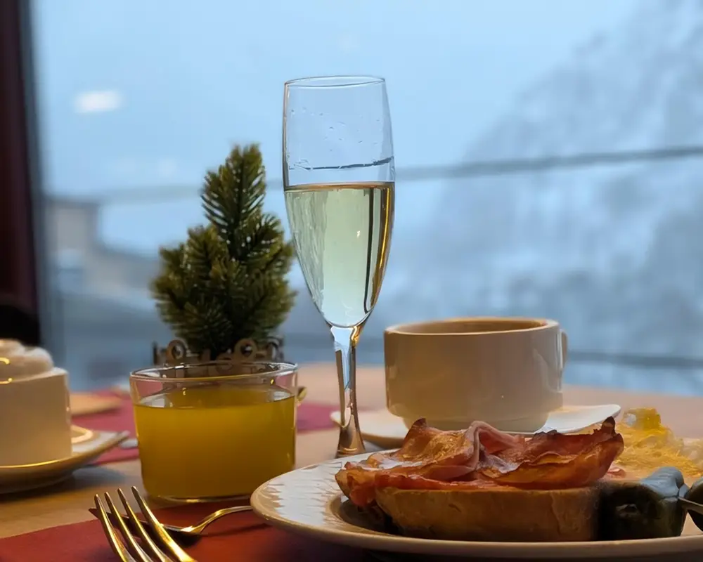Copa de champ&aacute;n con tostada y jam&oacute;n en mesa junto a ventana con caf&eacute;