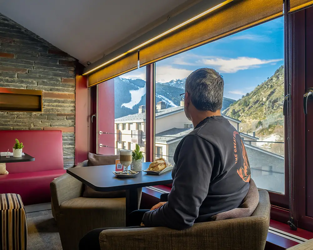 Hombre sentado en cafeter&iacute;a junto a la ventana, mirando monta&ntilde;as y valle