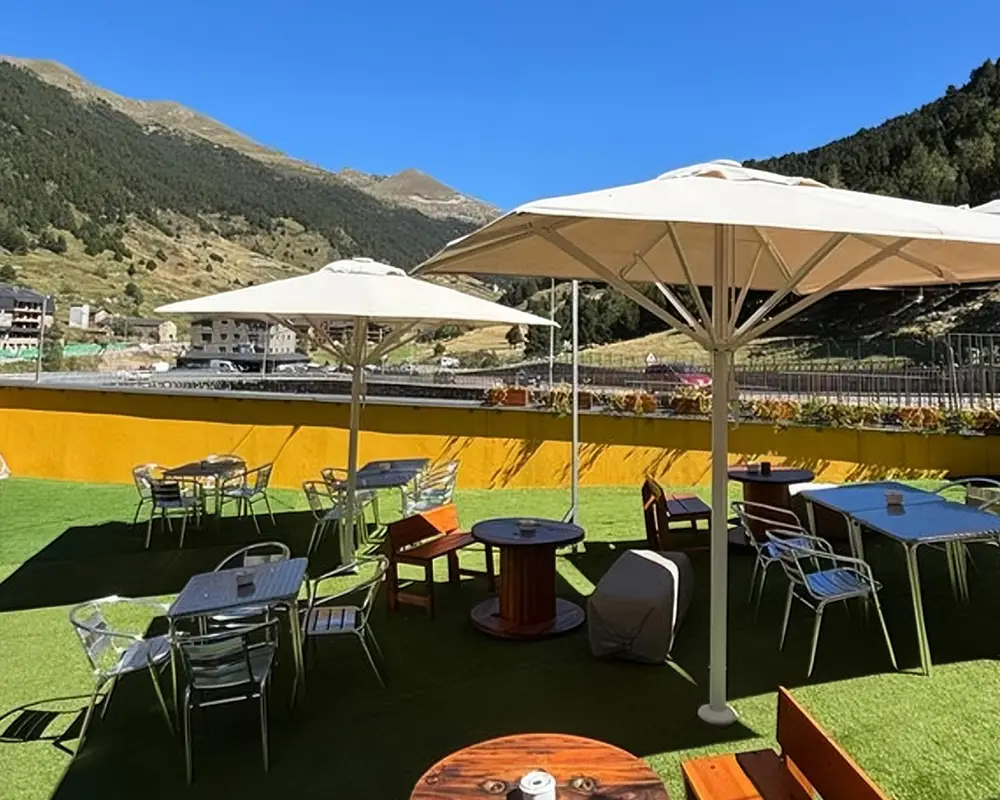 Terraza con mesas y sombrillas blancas en jard&iacute;n, rodeada de monta&ntilde;as