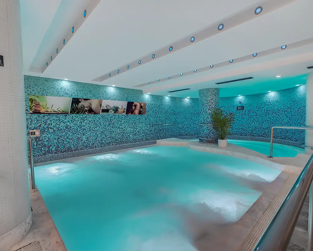 Piscina interior con paredes azulejadas turquesa y luces decorativas led.