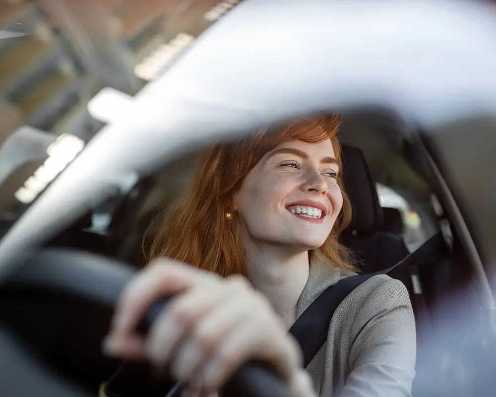Mujer sonriendo al volante en un coche, vista desde el asiento trasero