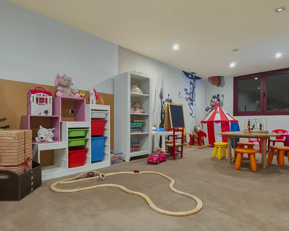Sala de juegos infantil con estanter&iacute;as, alfombra de riel y juguetes