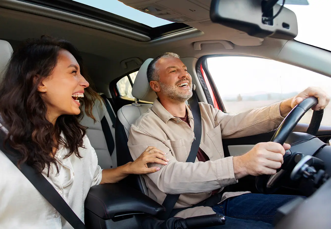 Pareja feliz conduciendo; mujer copiloto sonriente y hombre al volante