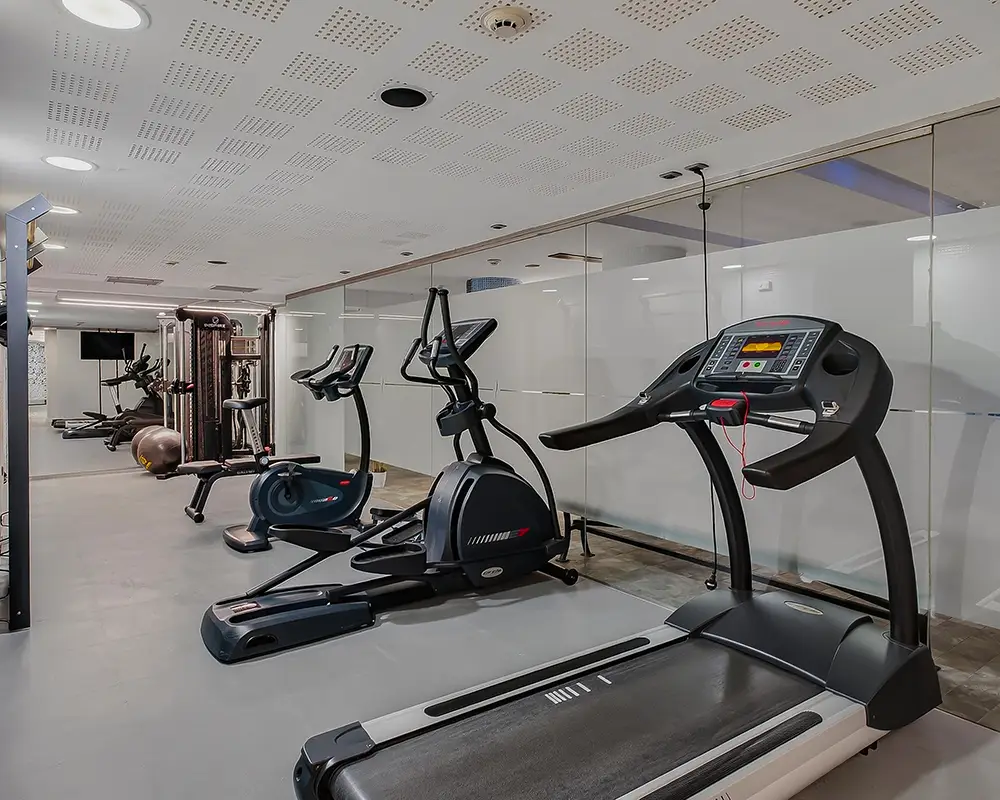 Gimnasio con m&aacute;quinas el&iacute;pticas y bicicleta est&aacute;tica bajo techo con luz blanca