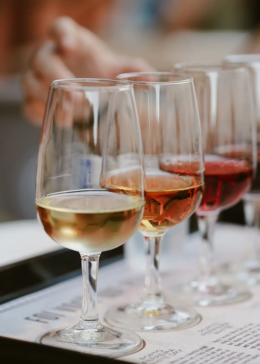 Copas con vino blanco y tinto en una mesa, con botellas al fondo.