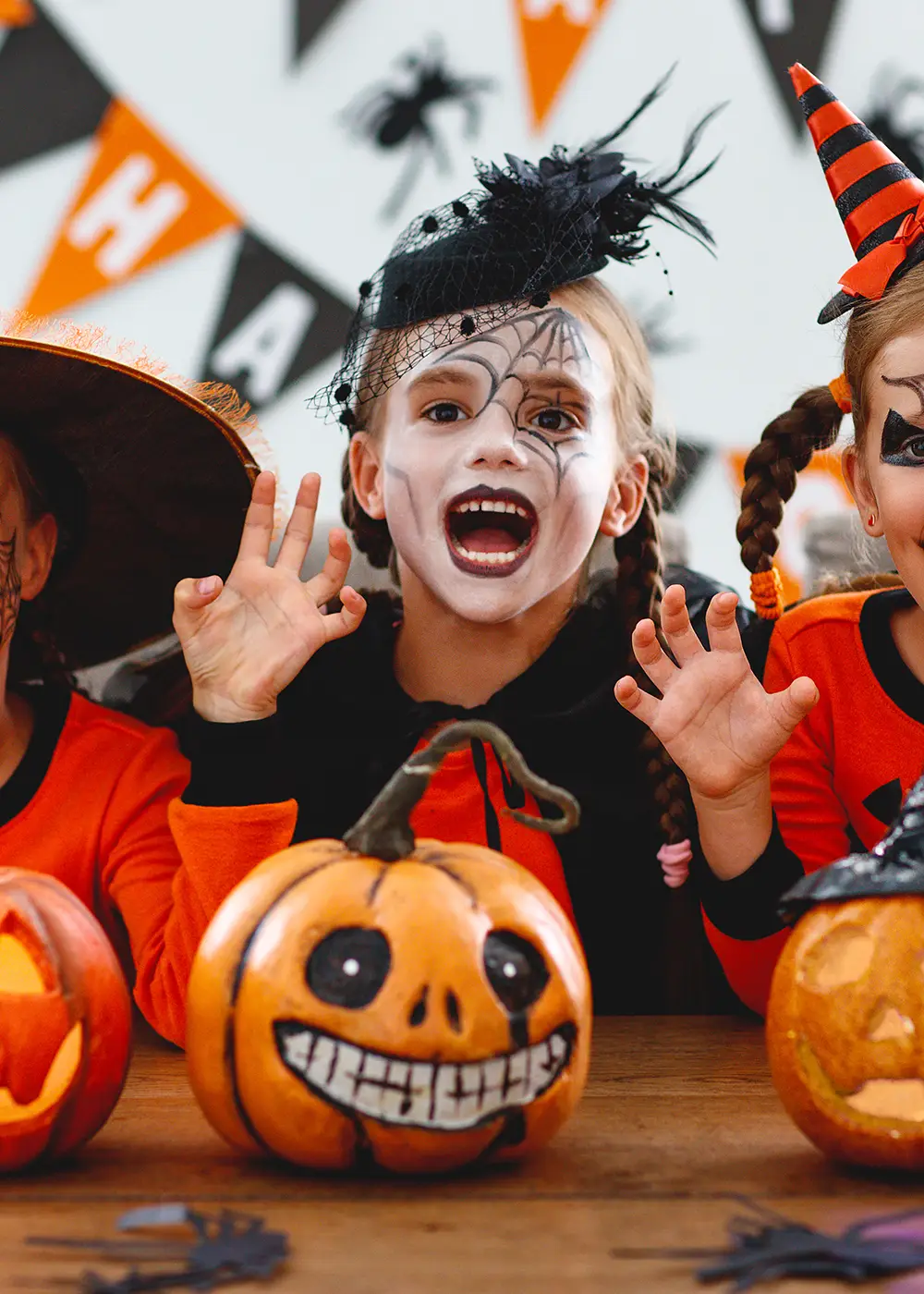 Ni&ntilde;os con maquillaje de Halloween saludan, con calabazas frente a ellos