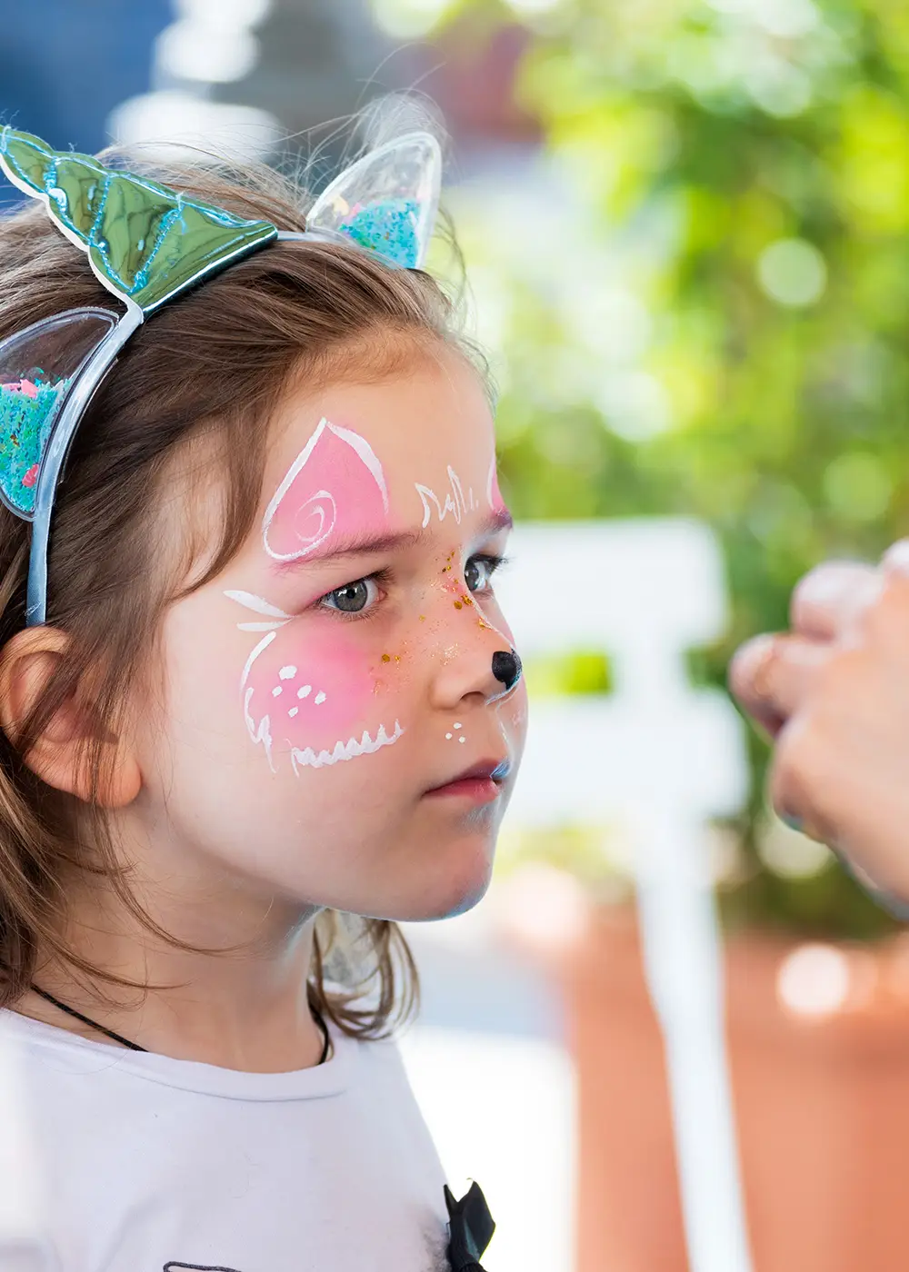 Ni&ntilde;a con maquillaje de fantas&iacute;a y orejas felinas, en jard&iacute;n, se&ntilde;alando