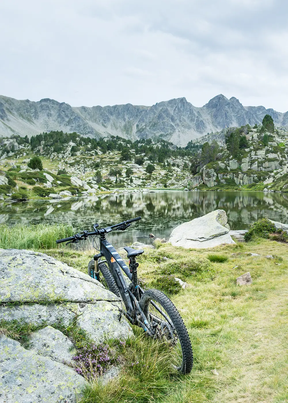 Bicicleta de monta&ntilde;a junto a lago con monta&ntilde;as y rocas al fondo