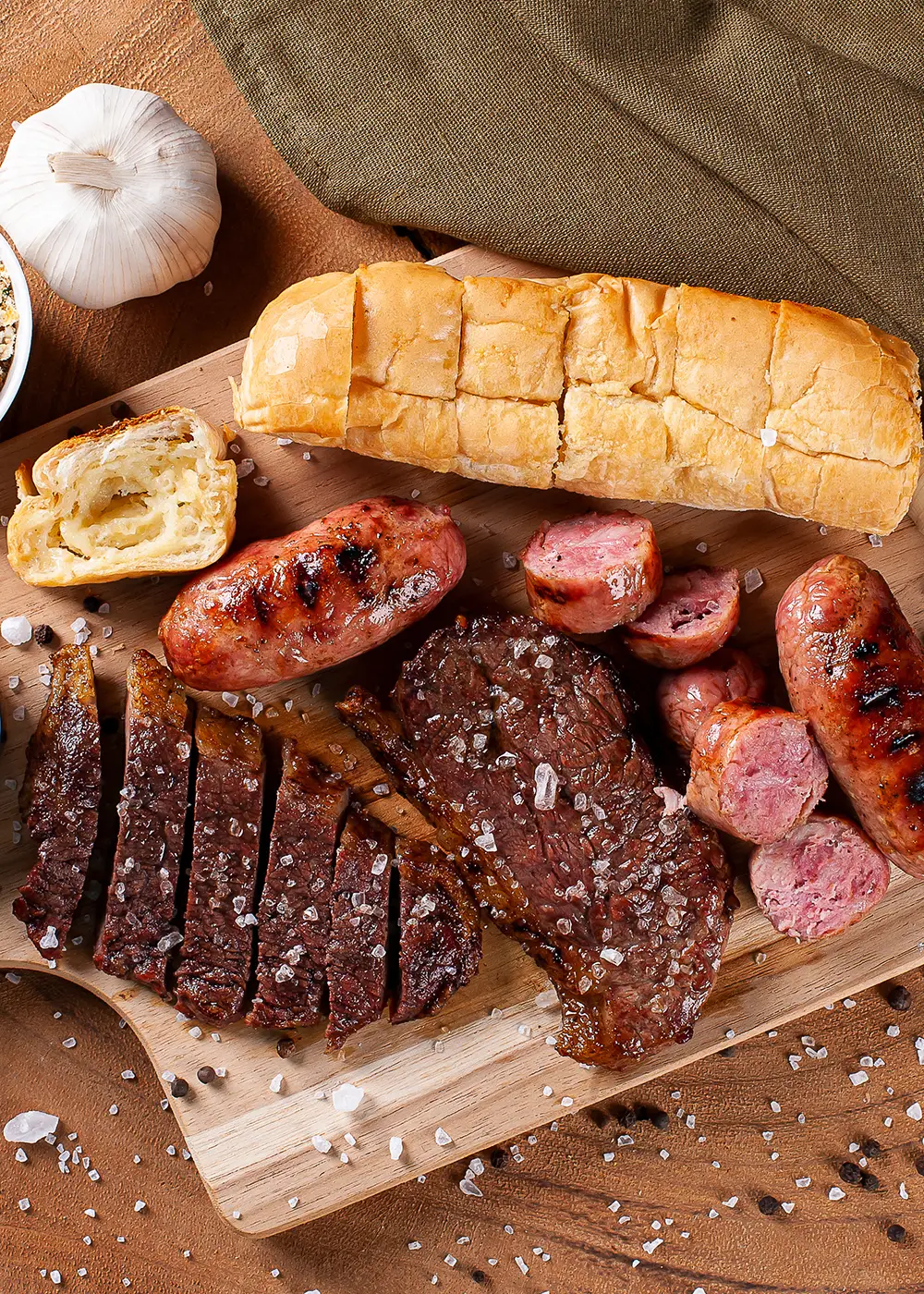 Tabla con salchichas y costillas asadas, pan de ajo y guarniciones, con sal.