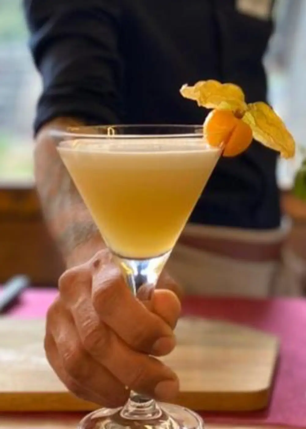 Persona sostiene un c&oacute;ctel amarillo con una decoraci&oacute;n de c&iacute;trico en vaso de martini.