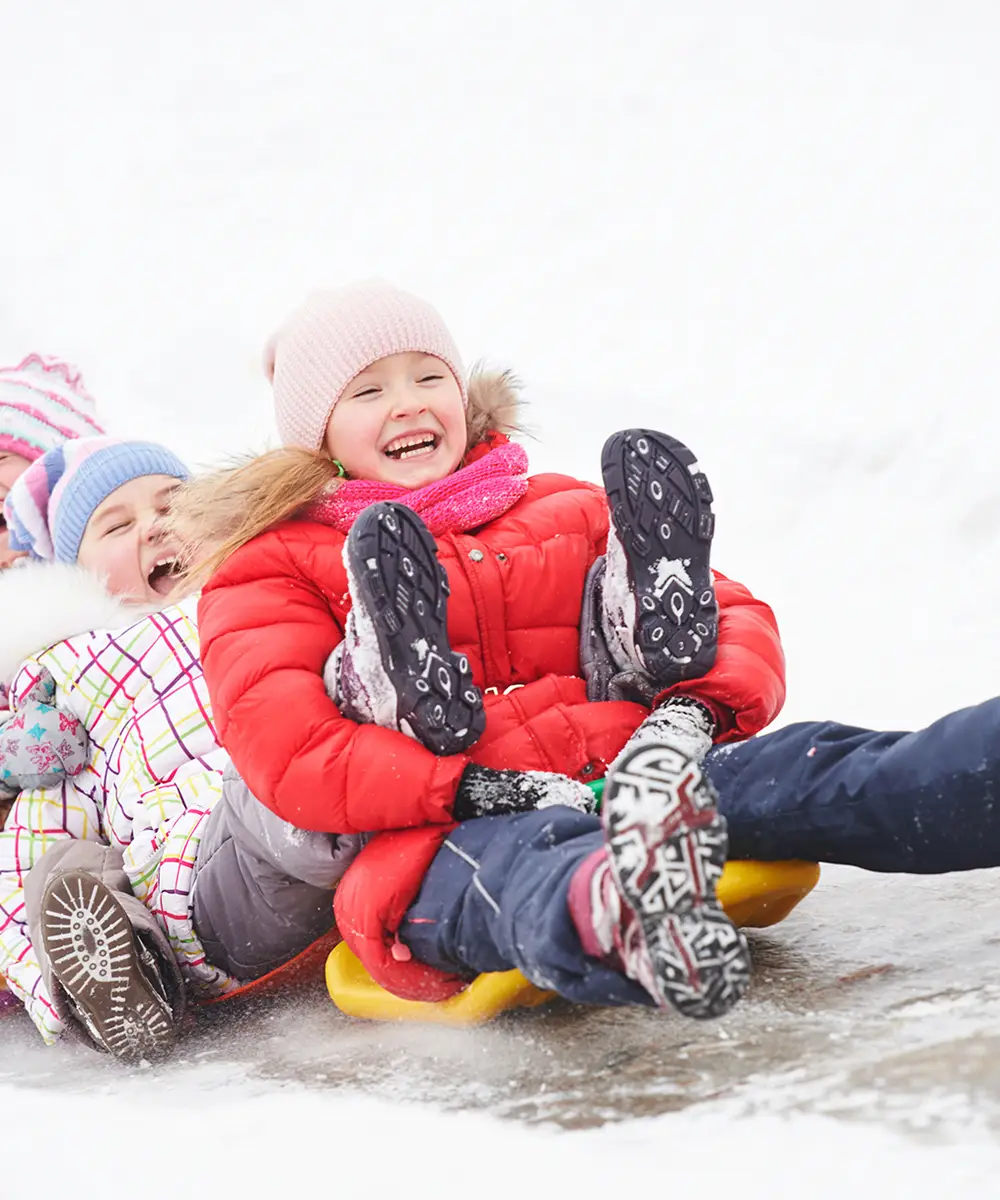 Ni&ntilde;as jugando en la nieve, abrazadas y riendo con botas.