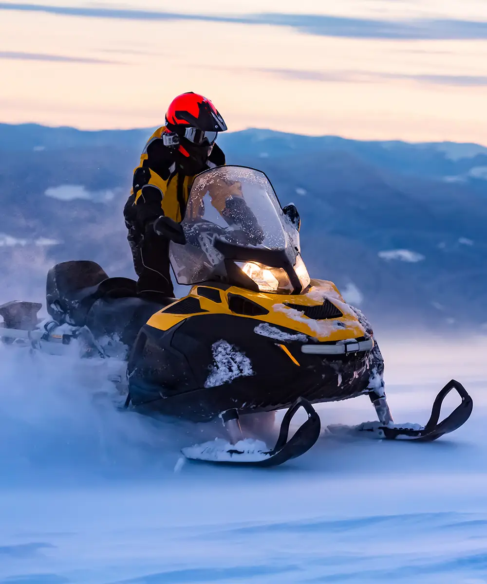 Motociclista en moto de nieve amarilla con casco rojo en paisaje nevado