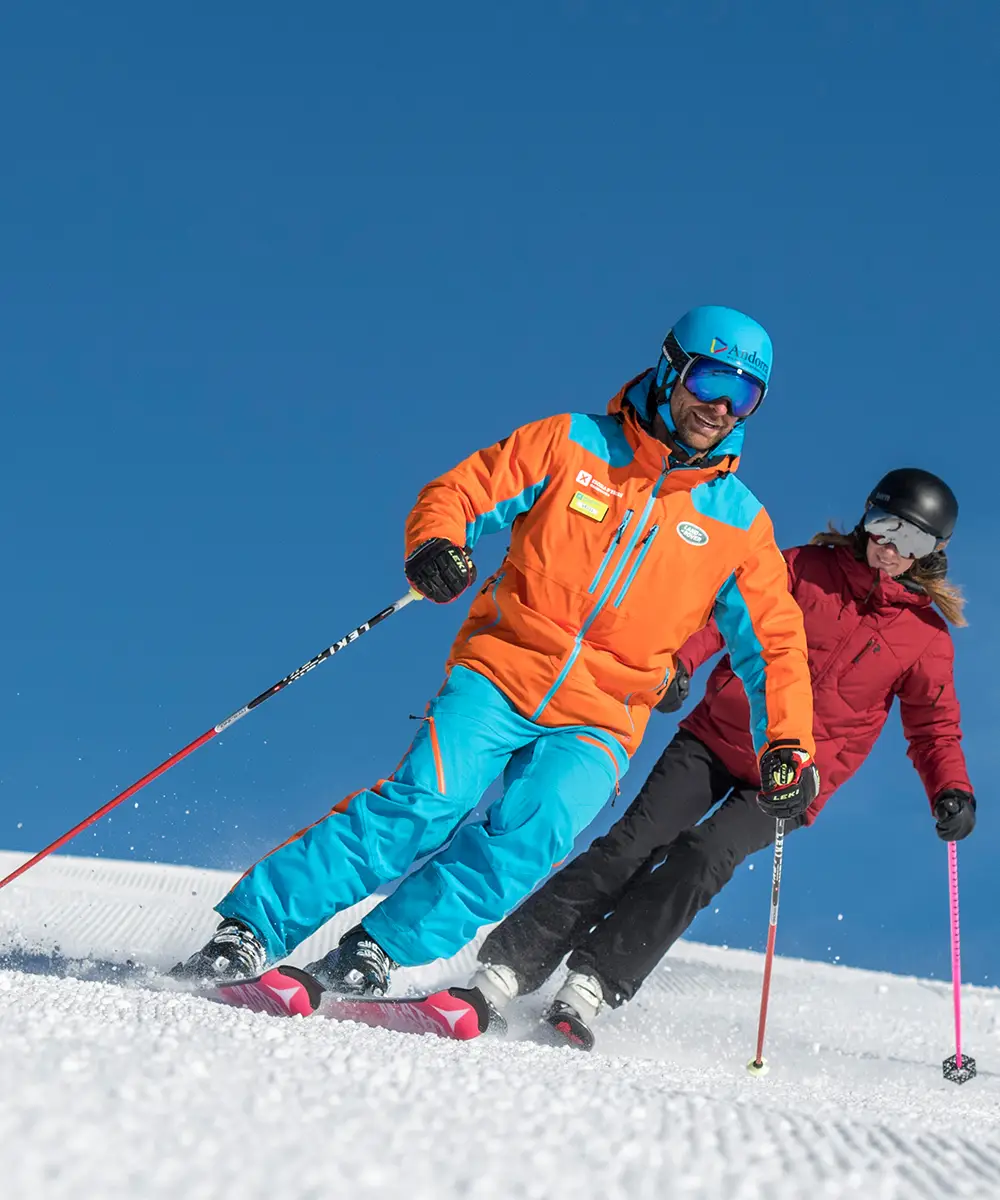Esquiadores con casco en la nieve, uno con chaqueta naranja y azul al cielo