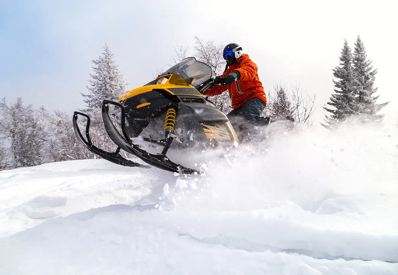 Conductor en trineo de motos de nieve, salpicando nieve en un bosque helado
