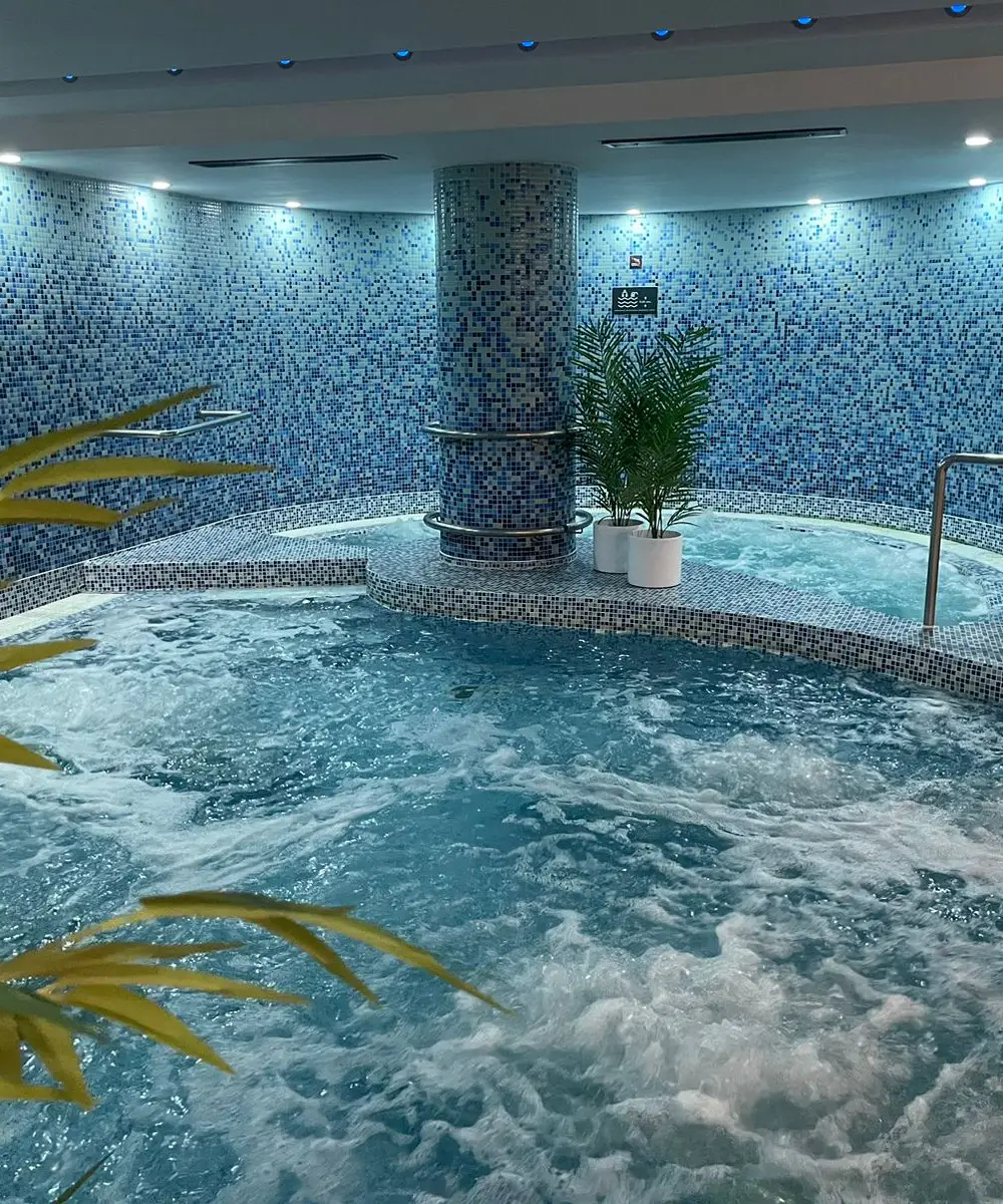 Piscina interior con jacuzzi y mosaicos azules, agua burbujeante