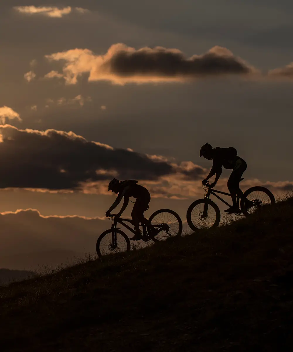 Dos ciclistas en bicicleta durante el atardecer, con nubes al fondo